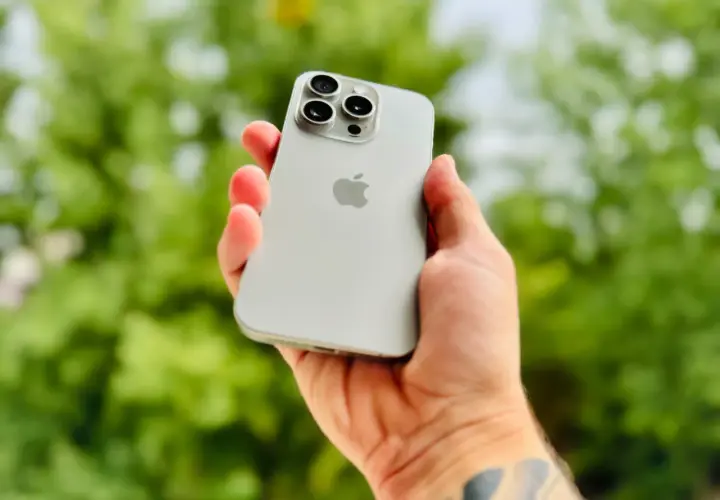 Dłoń trzyma srebrny iPhone 15 Pro Max, prezentując jego potężny aparat.