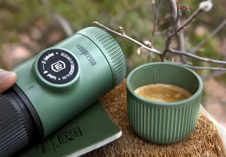 Zielona kawa w górach. Nanopresso i filiżanka świeżego espresso na drewnianym pniu, wśród gałązek. Idealny poranek w naturze.