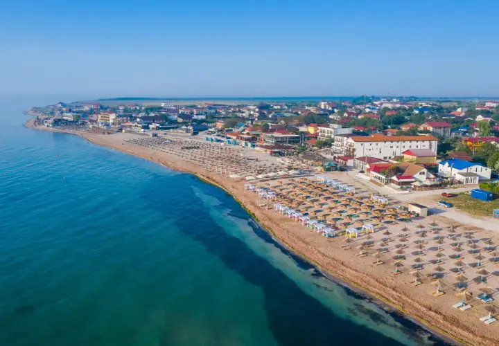 Plaża nad Morzem Czarnym z rzędami leżaków i parasoli. W tle zabudowania kurortu. Woda wygląda na ciepłą, idealną do kąpieli.