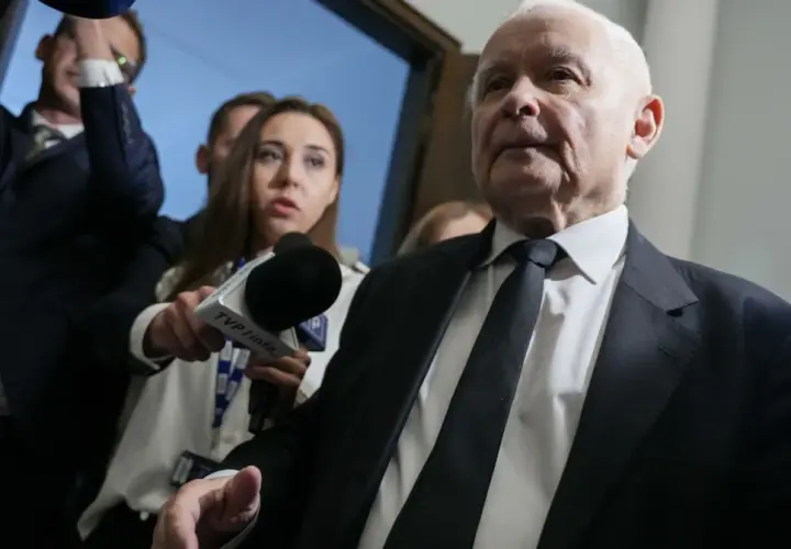 Starszy mężczyzna w garniturze, otoczony przez dziennikarzy z mikrofonem TVP Info, być może odpowiada na pytanie: co złego zrobił PiS?