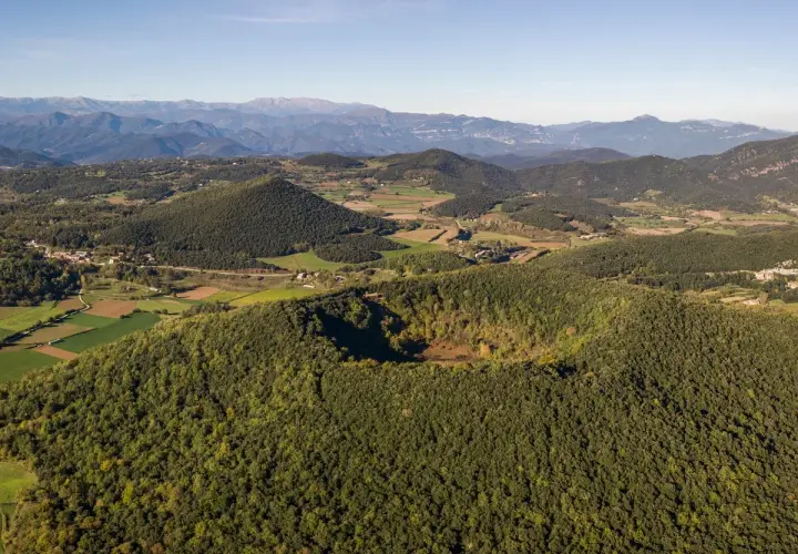 Paisaje aéreo de los volcanes de la Garrotxa, con conos volcánicos cubiertos de vegetación y un cráter visible.