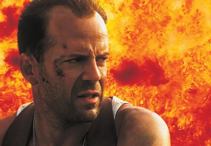 Bruce Willis i en actionfylld scen, med eld bakom sig. En klassisk bild från filmer med Bruce Willis.