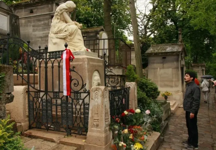 Pomnik na cmentarzu Père Lachaise z biało-czerwoną wstęgą. Mężczyzna wpatruje się w nagrobek.