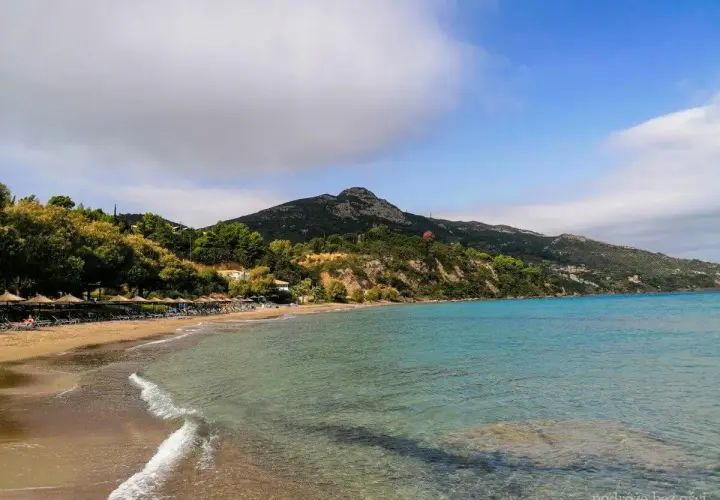 Piękna plaża Tragaki Zakynthos z turkusową wodą, zielonymi wzgórzami i rzędem leżaków pod parasolami.