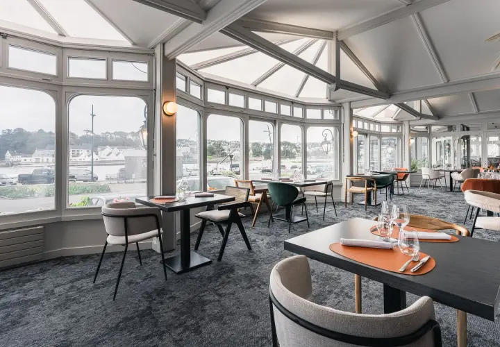 Salle de restaurant lumineuse avec vue sur le port, tables dressées et chaises modernes.