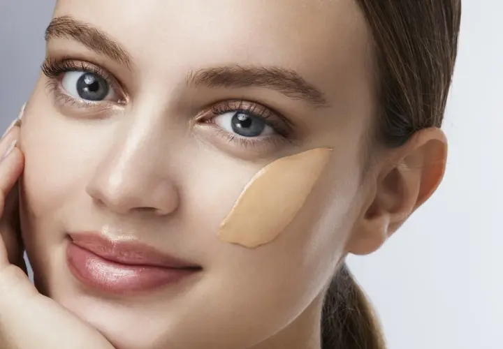 Una donna con un tocco di fondotinta sulla guancia, pronto per essere sfumato.