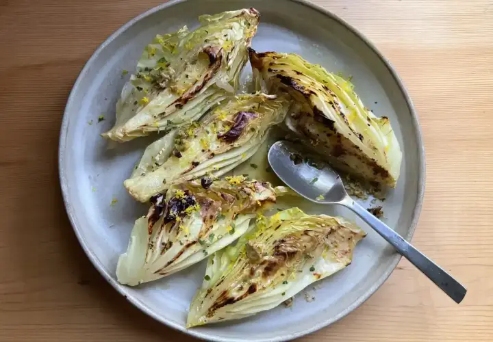 Grillad spetskål med citron och örter på en ljusgrå tallrik. En sked ligger på tallriken.