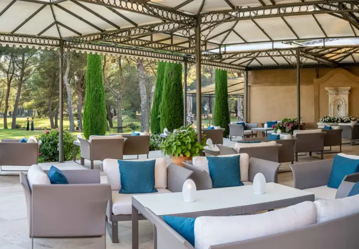 Terrasse de restaurant chic avec mobilier d'extérieur confortable et jardin verdoyant en arrière-plan.