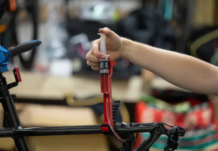 A hand uses a syringe filled with red fluid to bleed bicycle brakes. It's not as hard as you might think!