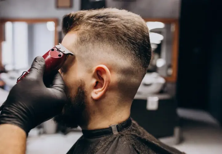 Barbero dando forma a un corte buzz cut fade con máquina. El cabello se desvanece suavemente de corto a largo.