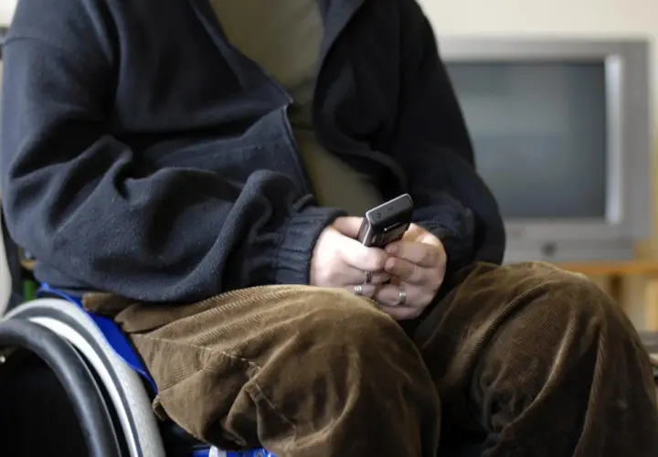 Osoba na wózku inwalidzkim, zmagająca się z atrofia mięśni, trzyma telefon.