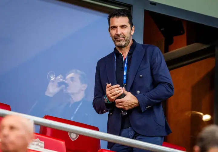 Gianluigi Buffon, legendarny włoski bramkarz, w eleganckim granatowym garniturze, obserwuje mecz z trybun.