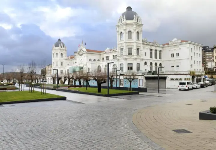 Edificio blanco con cúpulas en la plaza Italia Santander. Árboles desnudos y césped verde.