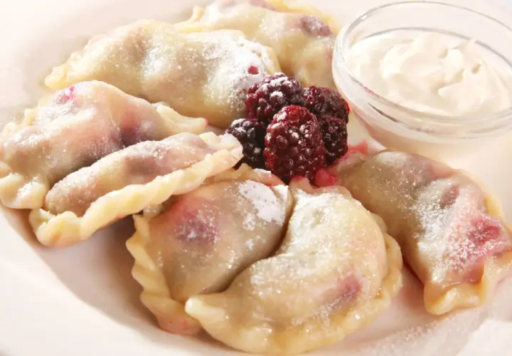 Pyszne pierogi z malinami, posypane cukrem pudrem, podane z kwaśną śmietaną i świeżymi owocami leśnymi.