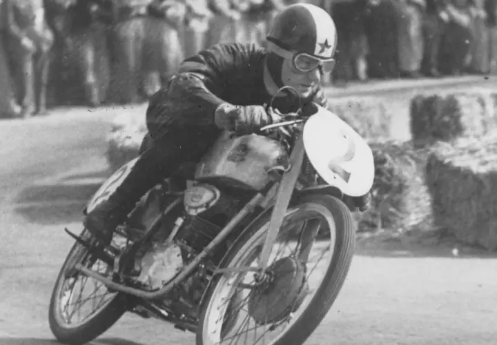 El piloto de carreras Carlo Ubbiali inclinado en su moto con el número 2, compitiendo con determinación.