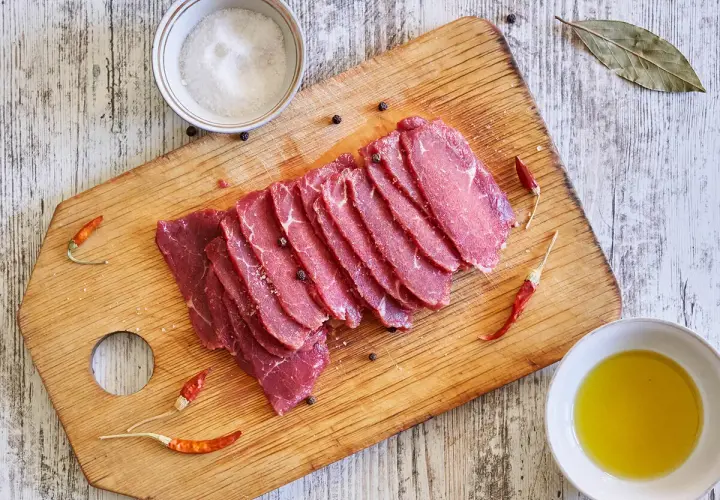 Filete de ternera crudo, cortado en finas lonchas, sobre tabla de madera con sal, pimienta, guindillas y aceite de oliva.