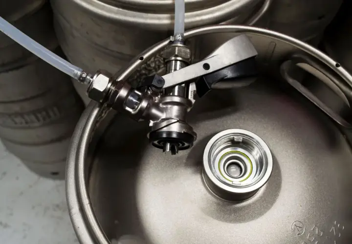 Metalowy keg piwa z podłączonym kranikiem i wężykiem. Gotowy do nalewania orzeźwiającego trunku.