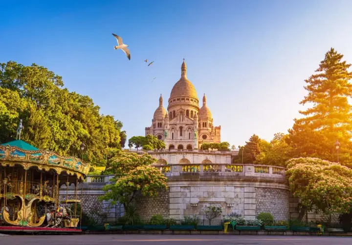 Bajkowy karuzela na tle bazyliki Sacré-Cœur na Montmartre. Mewy szybują na błękitnym niebie.