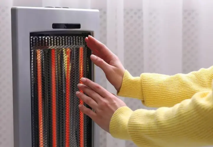 Manos cerca de un calentador eléctrico encendido. Las estufas eléctricas son peligrosas, ¡mantén la distancia!