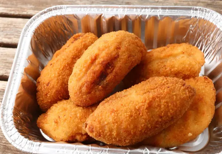 Croquetas de pollo doradas y crujientes en un recipiente de aluminio, listas para disfrutar.