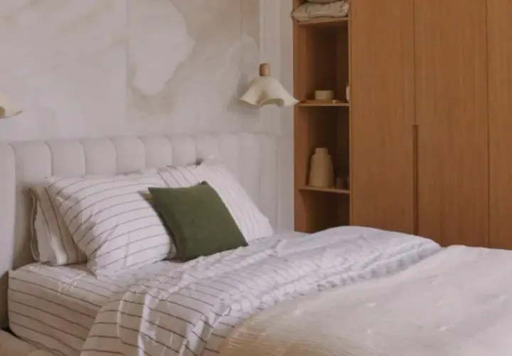 Lámparas colgantes de tela con forma de flor, ideales como tipo de luz para dormitorio, iluminan una cama con cabecero texturizado y ropa de cama a rayas.