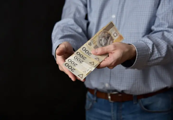 Mężczyzna w koszuli i jeansach podaje kilka banknotów po 200 zł. Może to być symbol zapłaty, darowizny lub cesji.