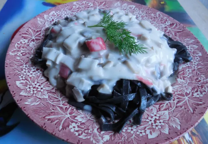 Czarny makaron z kremowym sosem i kawałkami kraba, udekorowany gałązką koperku. Pyszne danie na różowym talerzu.