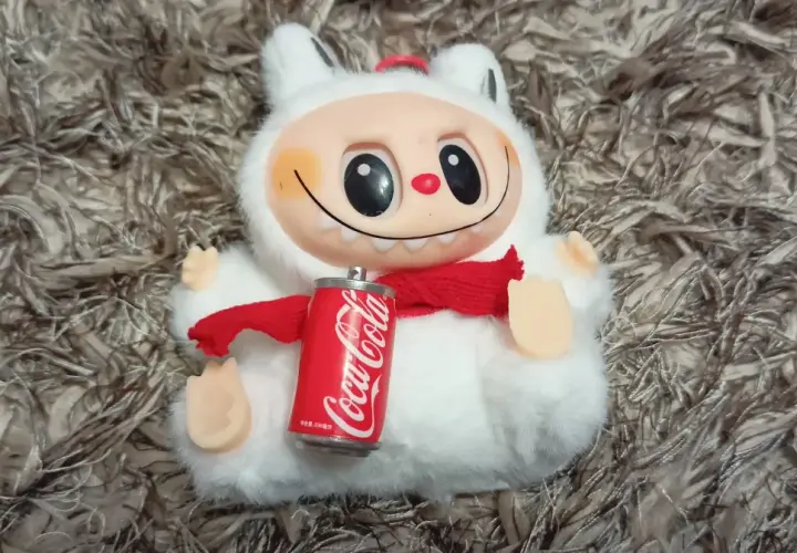 Pluszowy stworek z czerwoną szalikiem i puszką Coca-Coli, jakby to była największa zabawka na świecie.