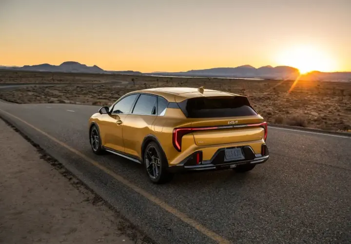 Un coche hatchback amarillo brillante recorre una carretera desierta al atardecer, con las montañas al fondo.