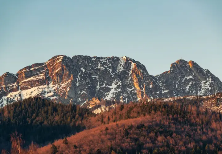 Giewont ośnieżony, z krzyżem na szczycie, w złotym świetle zachodzącego słońca. Czy ciężko wejść na Giewont? Widok zapiera dech w piersiach.