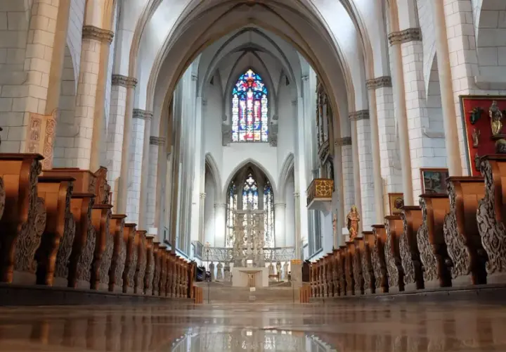 Blick durch das Kirchenschiff des Augsburger Doms mit seinen kunstvoll geschnitzten Holzbänken und dem farbenprächtigen Chorfenster.