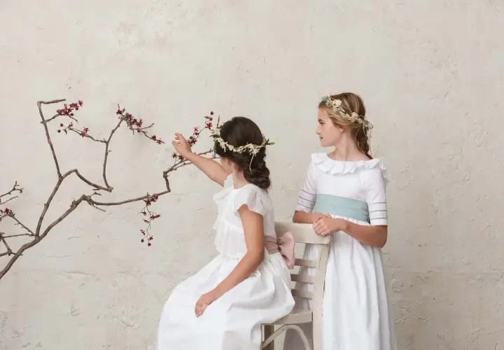 Dos niñas con peinados de comunión con diadema floral, una sentada tocando ramas, la otra de pie.
