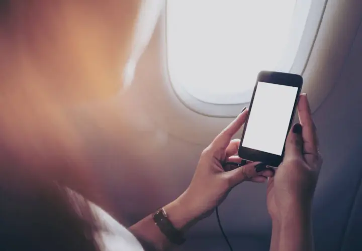 Ręce trzymające smartfon z pustym ekranem, siedząc przy oknie samolotu. Zastanawiasz się, czy bez karty SIM można dzwonić?