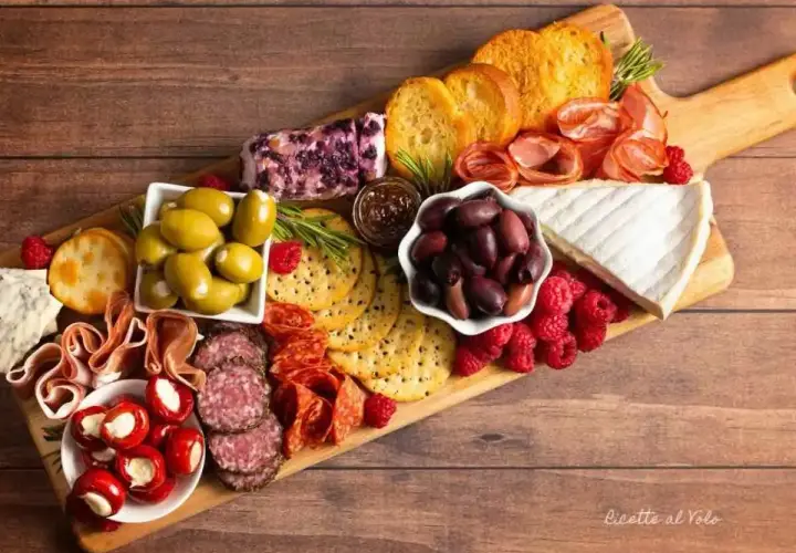 Tagliere ricco di antipasti sfiziosi: salumi, formaggi, olive, lamponi e crostini. Un tripudio di sapori e colori.