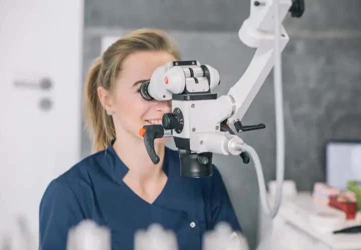 Dentystka wykonuje leczenie kanałowe pod mikroskopem, precyzyjnie pracując z użyciem nowoczesnego sprzętu.
