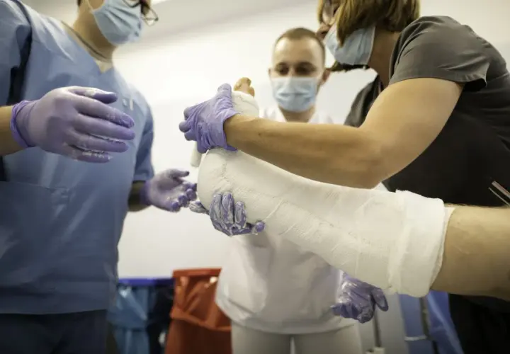 Trzech lekarzy w maseczkach i rękawiczkach zakłada gips na nogę pacjenta.