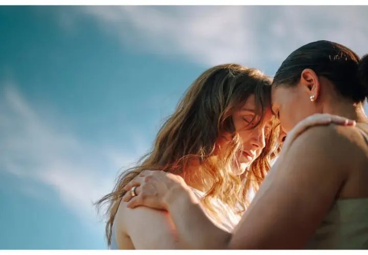 Due donne si abbracciano con dolcezza, un'immagine che evoca il vero amore platonico, significato di profonda connessione spirituale sotto un cielo azzurro.
