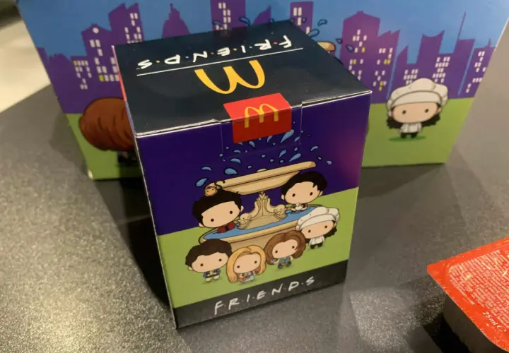 Pudełko McDonald's z motywem Friends, przedstawiające urocze postacie z serialu przy fontannie.