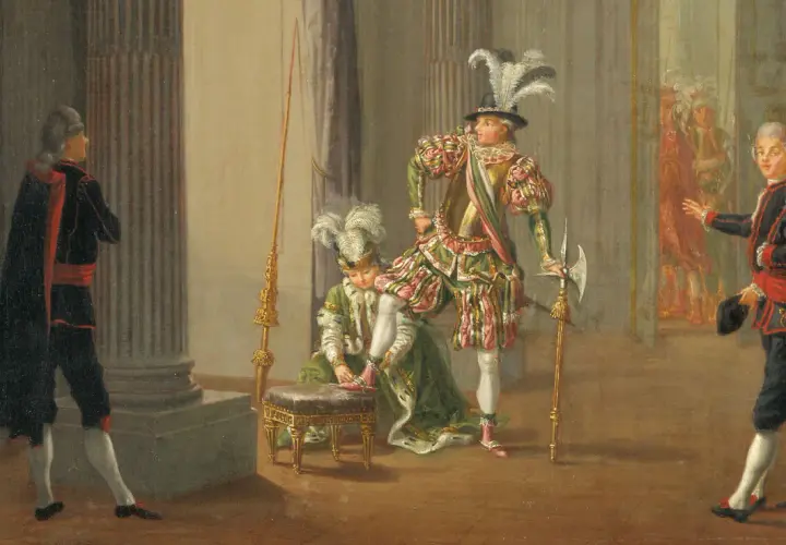 Scen från teater kungen där en person får sina skor på sig. Flera figurer i historiska dräkter.