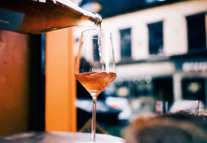 En flaska häller upp ett bubbligt, roséfärgat pet nat i ett elegant glas. En härlig kväll väntar.