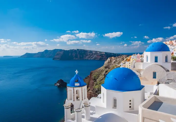 Santorini, idealne miejsce na wakacje w listopadzie gdzie najcieplej. Białe domy z niebieskimi kopułami nad lazurowym morzem.