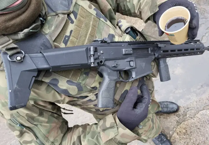 Żołnierz w kamuflażu trzyma karabin i kubek kawy. Czy to broń kolekcjonerska czy sportowa?