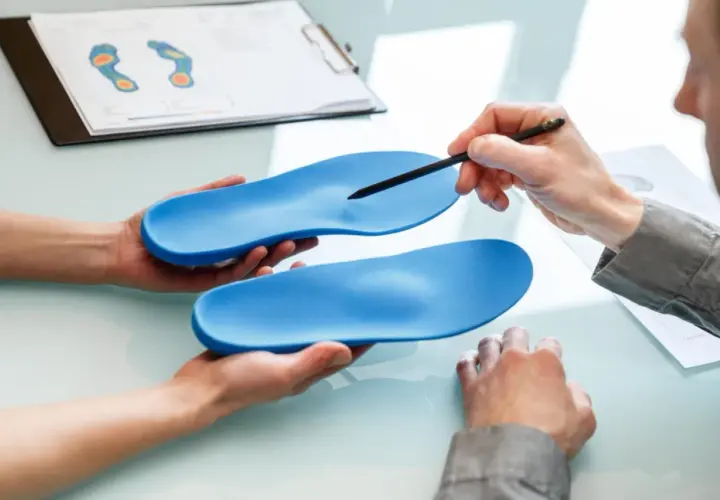 Beratung zu orthopädische einlagen kostenübernahme. Hände halten blaue Einlagen, ein Stift zeigt auf eine. Fußdruckanalyse im Hintergrund.