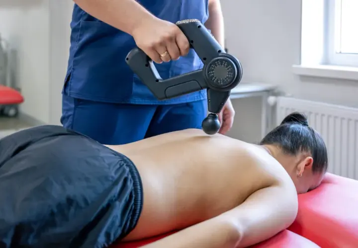 Fizjoterapeuta wykonuje masaż wibracyjny pleców. Choć zazwyczaj przynosi ulgę, warto pamiętać o potencjalnych masaż wibracyjny skutki uboczne.