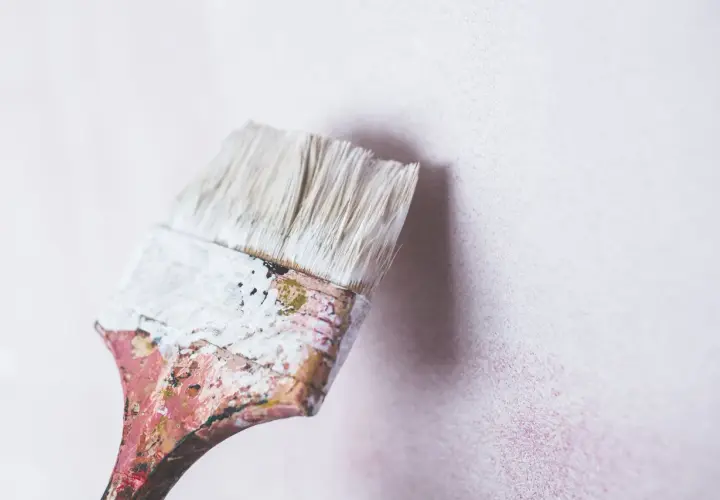 Brocha desgastada con pintura blanca lista para renovar una pared. Se puede pintar encima de pintura de caucho.