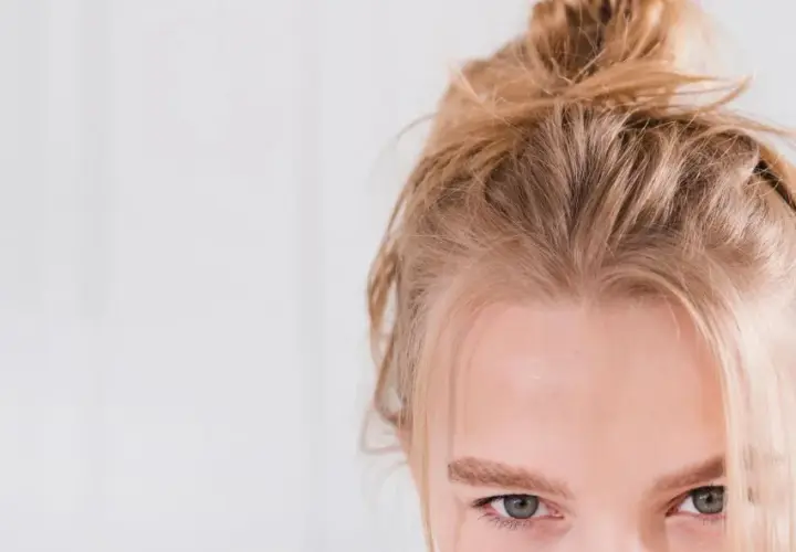 En ung kvinna med kall blond frisyr i en slarvig knut. Hennes gröna ögon möter betraktaren.