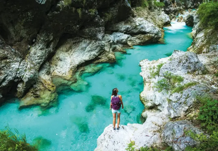 Wanderin am Juliana Trail: Eine Frau mit Rucksack steht auf einem Felsen und blickt auf das türkisfarbene Wasser einer Schlucht.