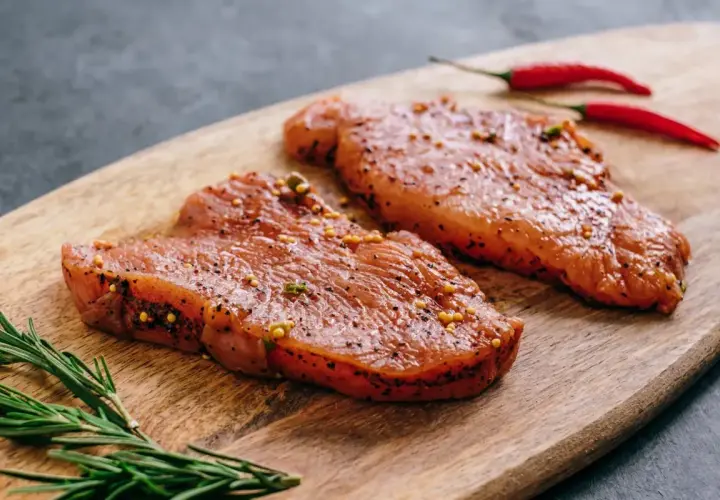 Dwa kawałki indyka w marynacie z gorczycą i pieprzem, obok gałązka rozmarynu i dwa czerwone chili.