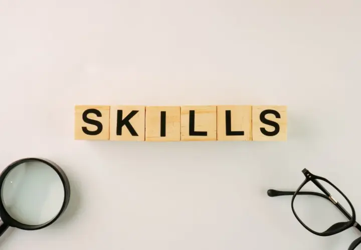 Wooden blocks spell "SKILLS." A magnifying glass and glasses suggest an organization leader carefully assessing talents.