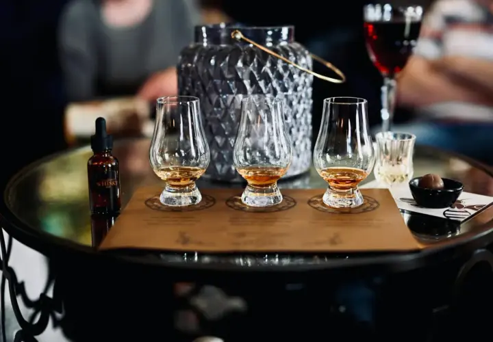 Degustacja whisky metodą tulipana: jak poczuć torf, wanilię i dym. Na stole kieliszki, buteleczka z whisky i czekoladka.